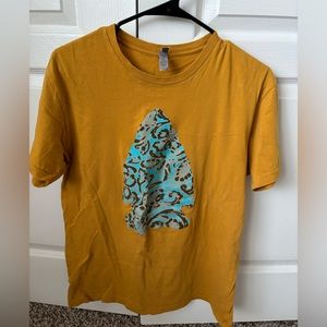 Mustard yellow short sleeve top with a blue arrow head in the middle, medium